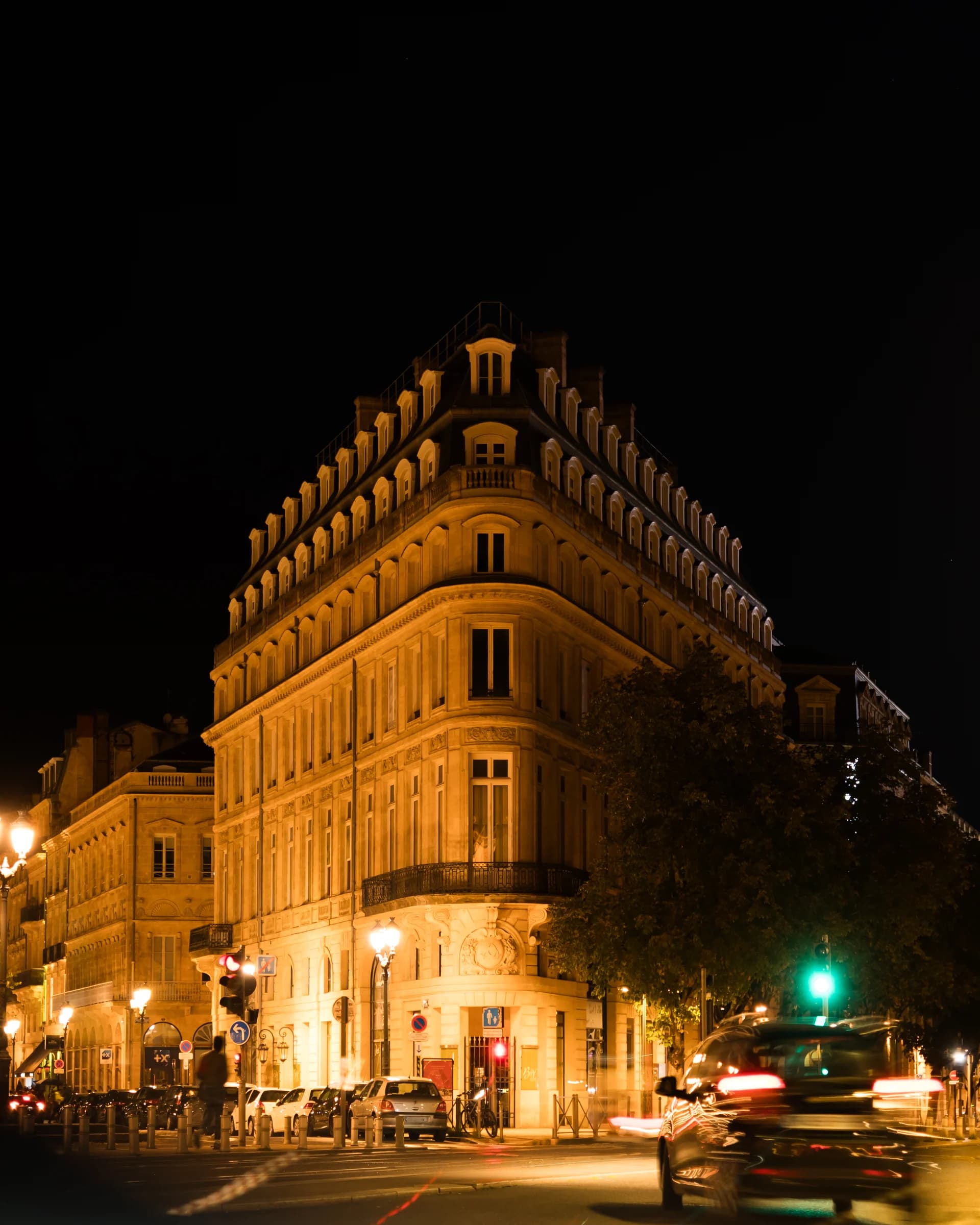 Before: A corner building in Bordeaux at night under orange street lamps, with a car driving past