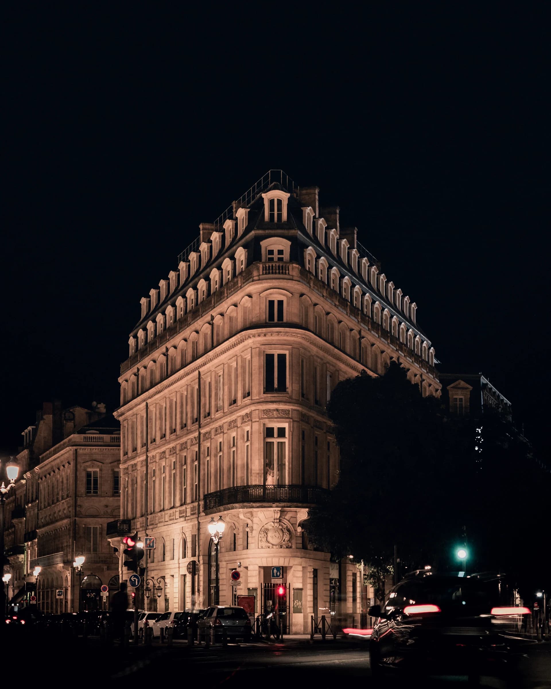 After: A corner building in Bordeaux at night under orange street lamps, with a car driving past